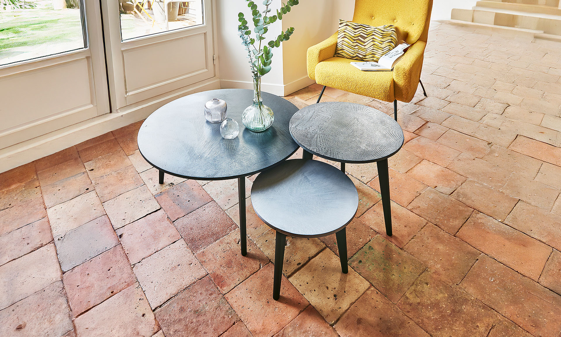 Photo d'ambiance présentant une table basse ronde, un coin canapé rond et un guéridon rond. Toutes les tables ont un dessus en finitions béton et un piétement en hêtre massif finition noire mate.